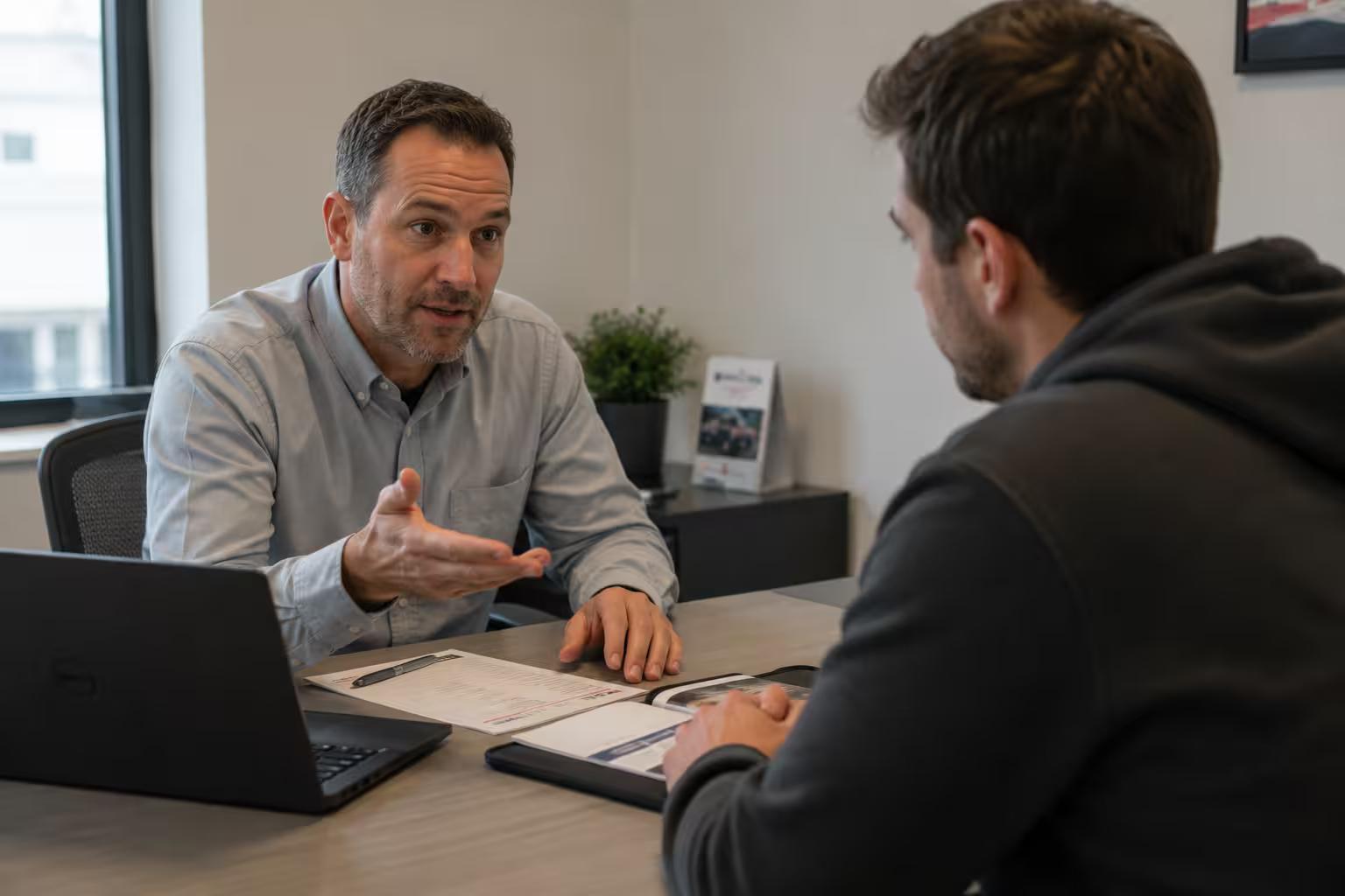 Conseiller en financement automobile, main ouverte, expliquant les critères d'approbation à un client assis en face de lui